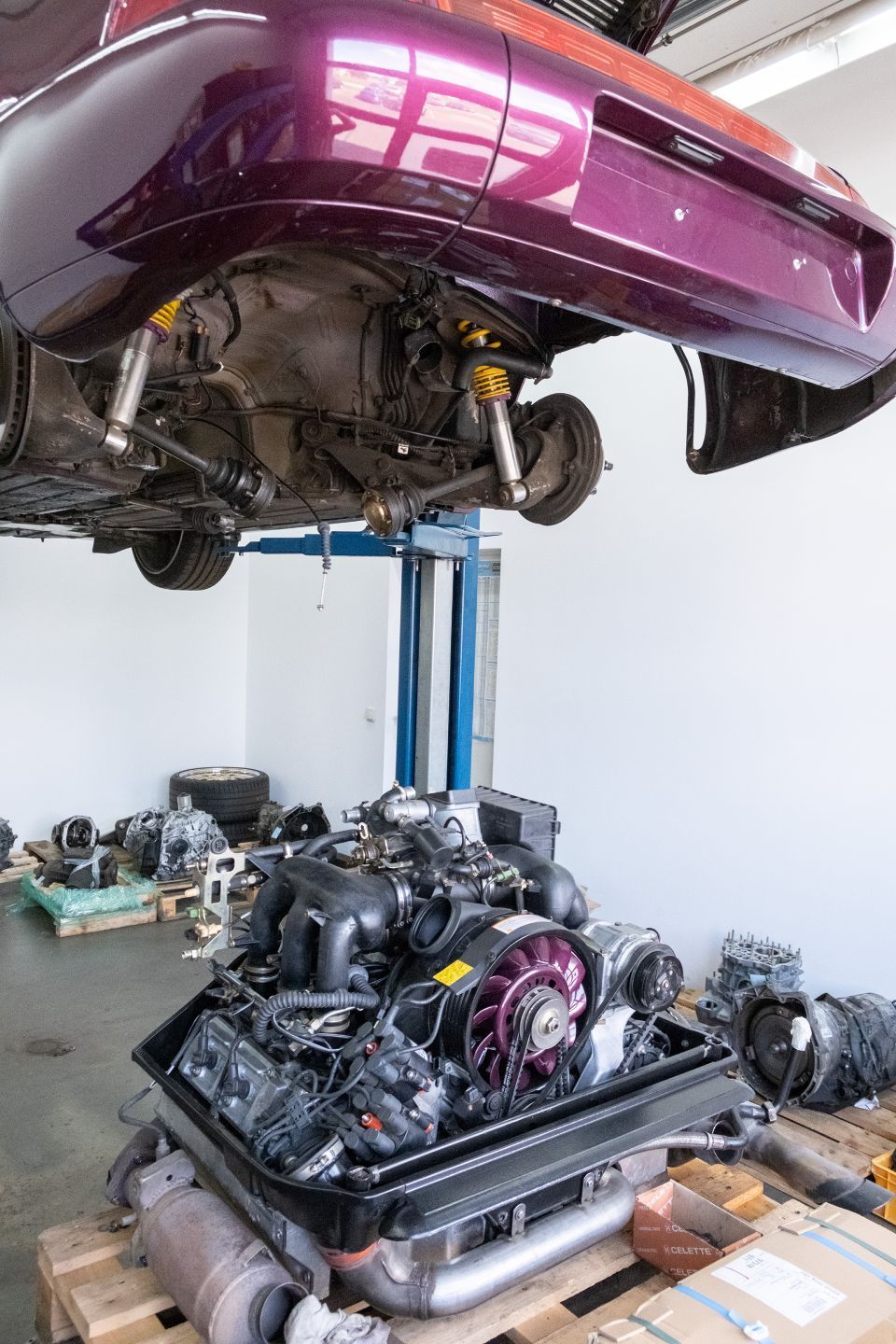 Das Auto steht auf einer Hebebühne, der Motor ist ausgebaut; Motor und Teile befinden sich in einem Behälter darunter.