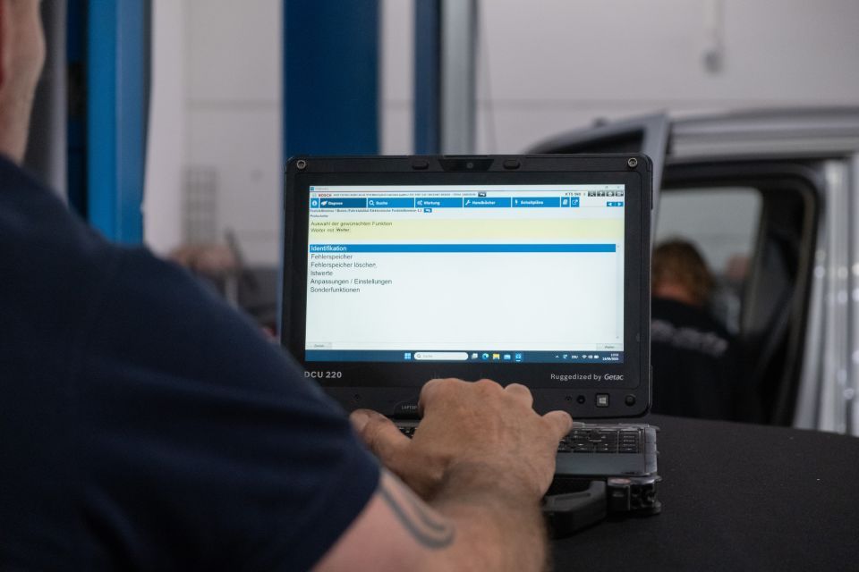 Mechaniker benutzt Laptop zur Diagnose eines Fahrzeugs in einer Werkstatt.