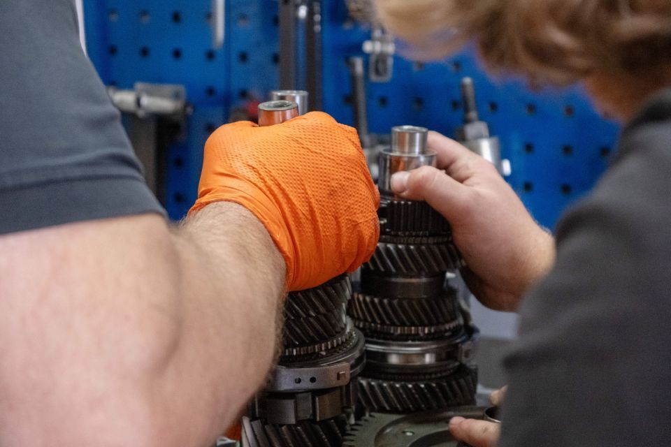 Eine Person mit orangefarbenem Handschuh arbeitet in einer Werkstatt an einem Getriebe.