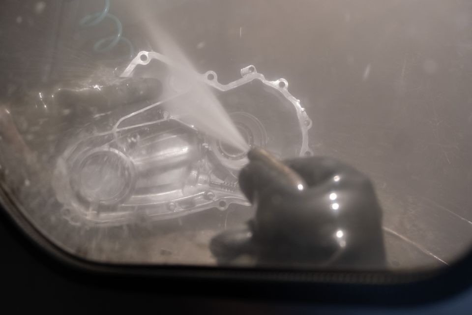 Eine Person benutzt in einem Schrank einen Sandstrahler an einem Autoteil.