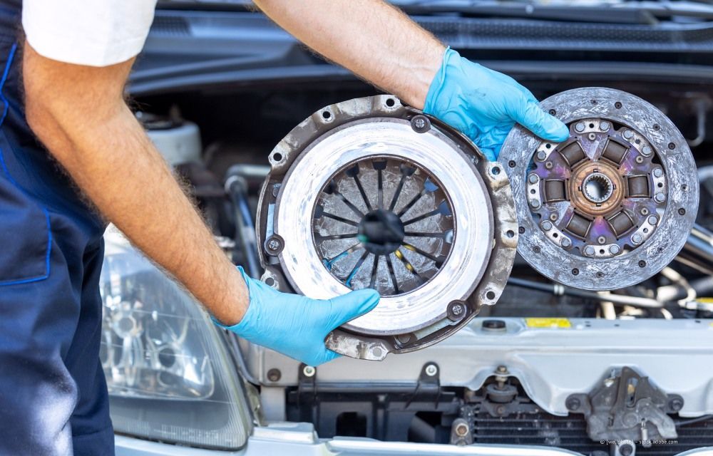 Ein Mechaniker hält eine neue und eine abgenutzte Kupplungseinheit in der Nähe einer geöffneten Motorhaube.