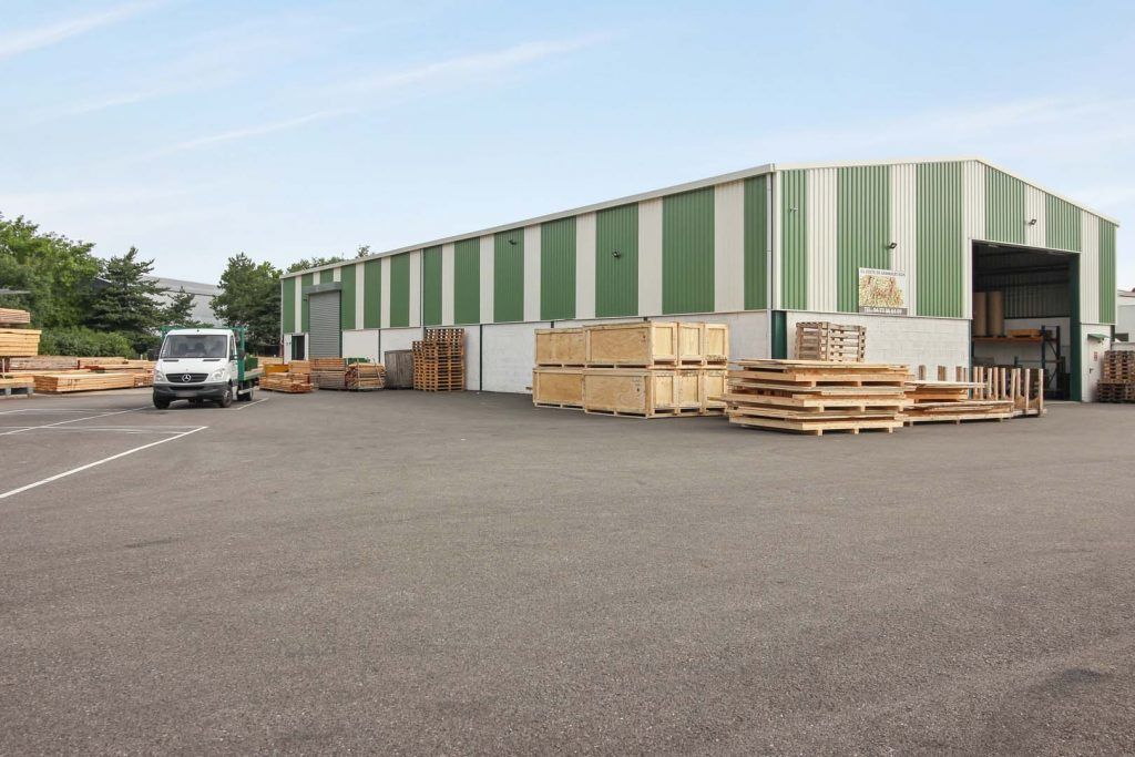 Entrepôt à façade verte et blanche. Palettes de bois et camionnette sur l'asphalte.