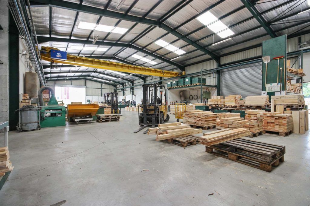 Intérieur d'un entrepôt avec chariot élévateur, palettes et machines, sous un toit métallique.