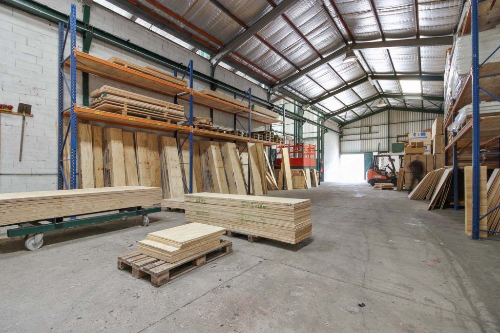 Intérieur d'entrepôt rempli de bois et d'étagères. Un chariot élévateur et un sol en béton sont visibles.