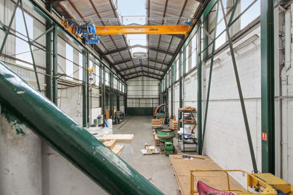 Intérieur d'un entrepôt industriel avec pont roulant, tuyauterie verte et divers équipements.