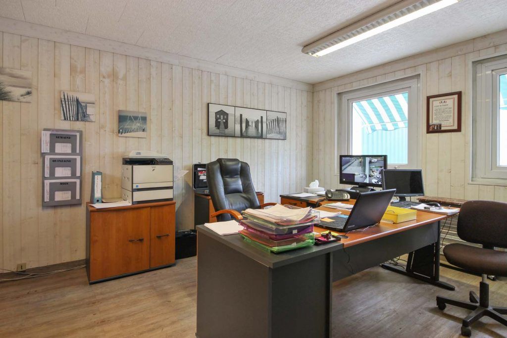 Intérieur de bureau avec bureau, chaise, ordinateur, imprimante et documents. Lambris clair aux murs.