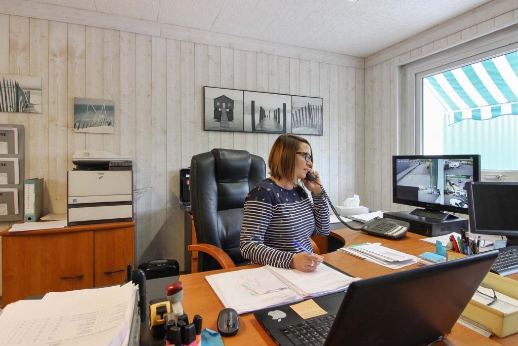 Femme assise à son bureau, au téléphone, regardant son écran d'ordinateur, en train de travailler.
