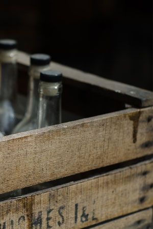 Caisse en bois contenant des bouteilles en verre vides. Ambiance sombre.