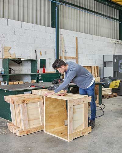 Un homme travaille le bois dans un atelier, en train d'assembler une boîte en bois.