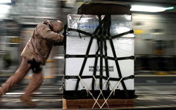 Une personne pousse une grande caisse sanglée dans un décor intérieur flou.