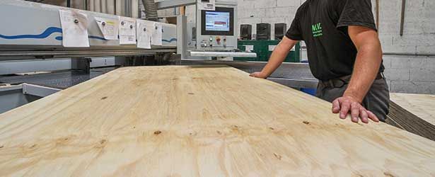 Une personne travaille le bois dans une usine. Une grande plaque de bois est manipulée près d'une machine.