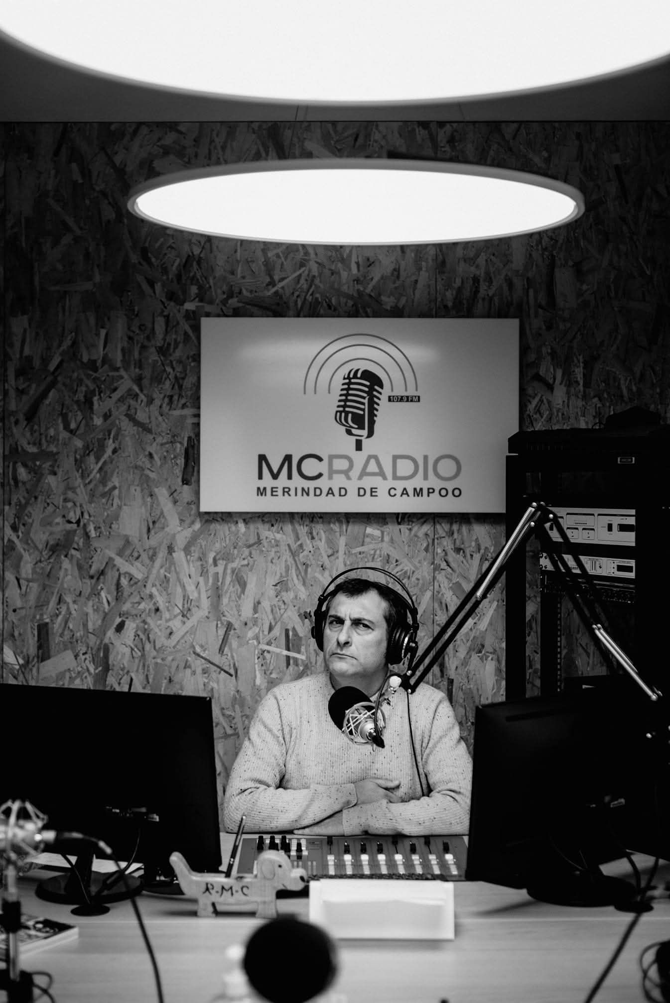Hombre en un estudio de radio con auriculares, micrófono y mesa de mezclas. Detrás, un cartel dice 
