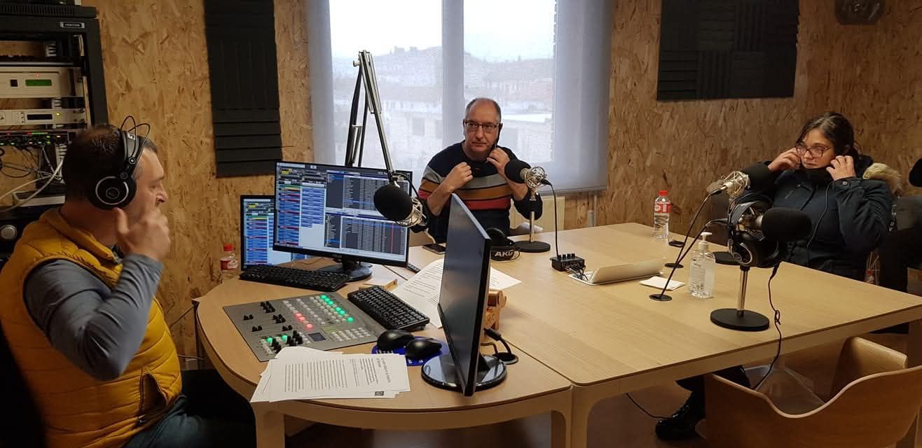 Tres personas en una mesa en un estudio con micrófonos, computadoras y una mesa de sonido.