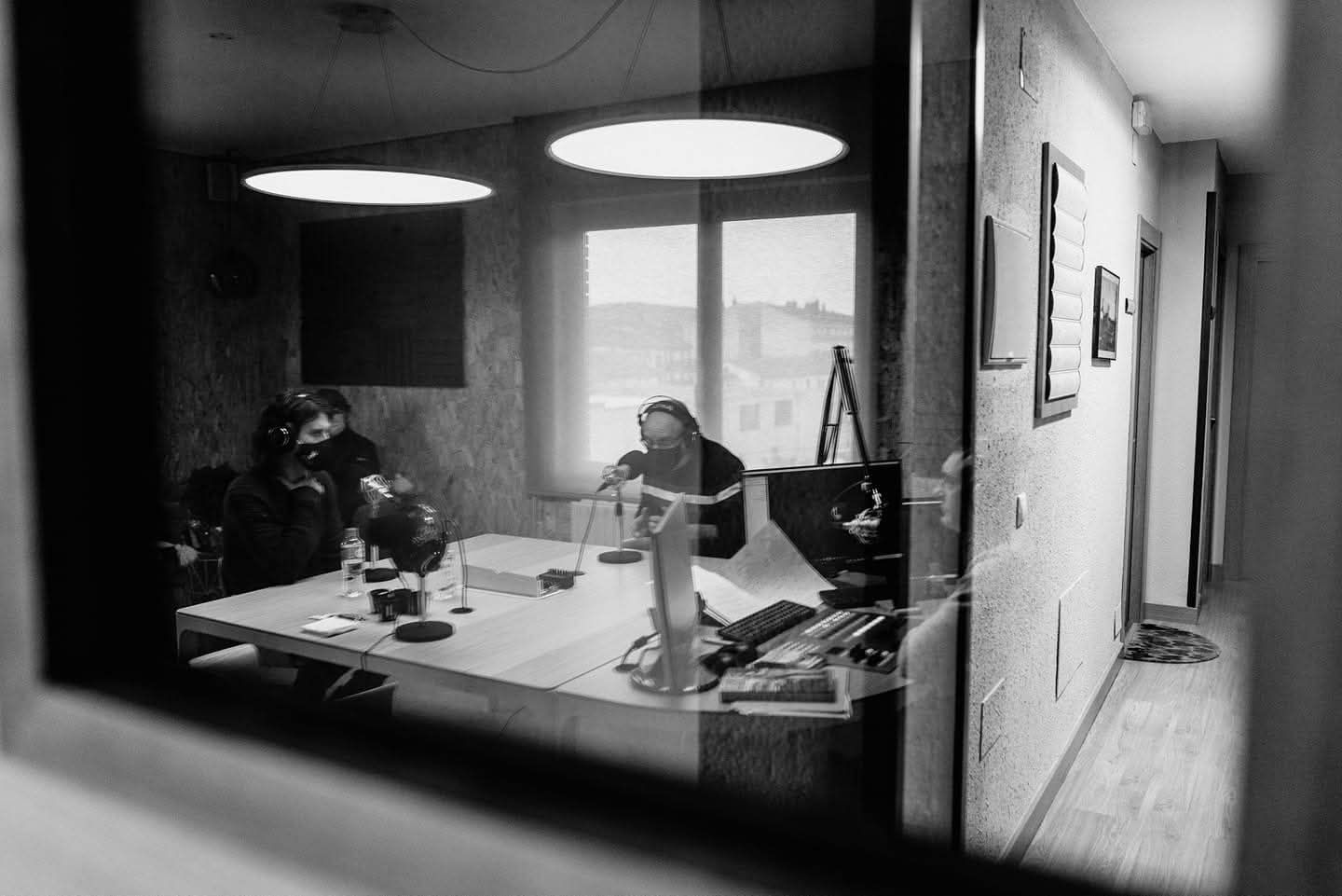 Fotografía en blanco y negro de personas sentadas en una mesa en una habitación, vistas a través de una ventana.