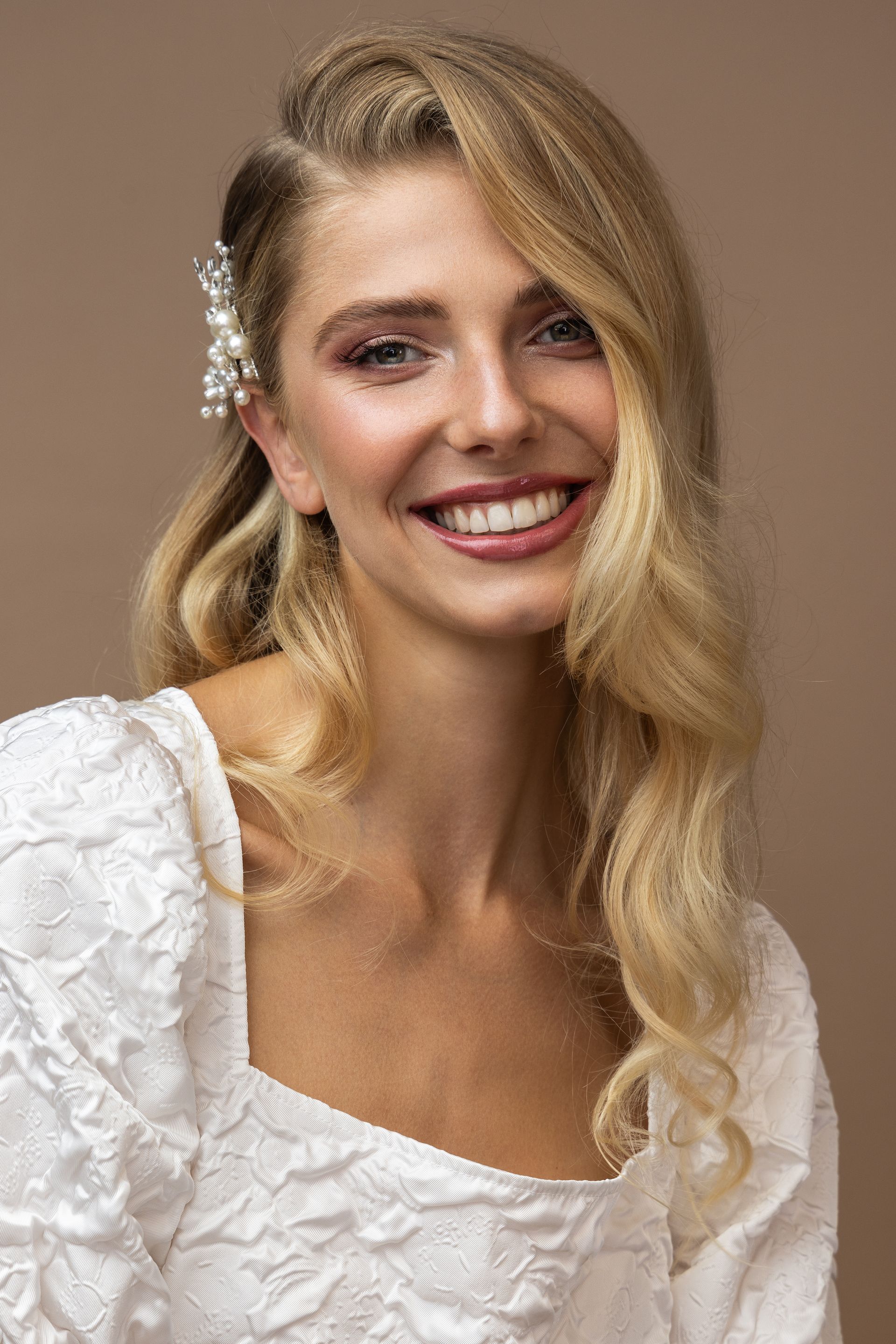 Eine Frau in einem weißen Kleid lächelt und trägt eine Haarspange.