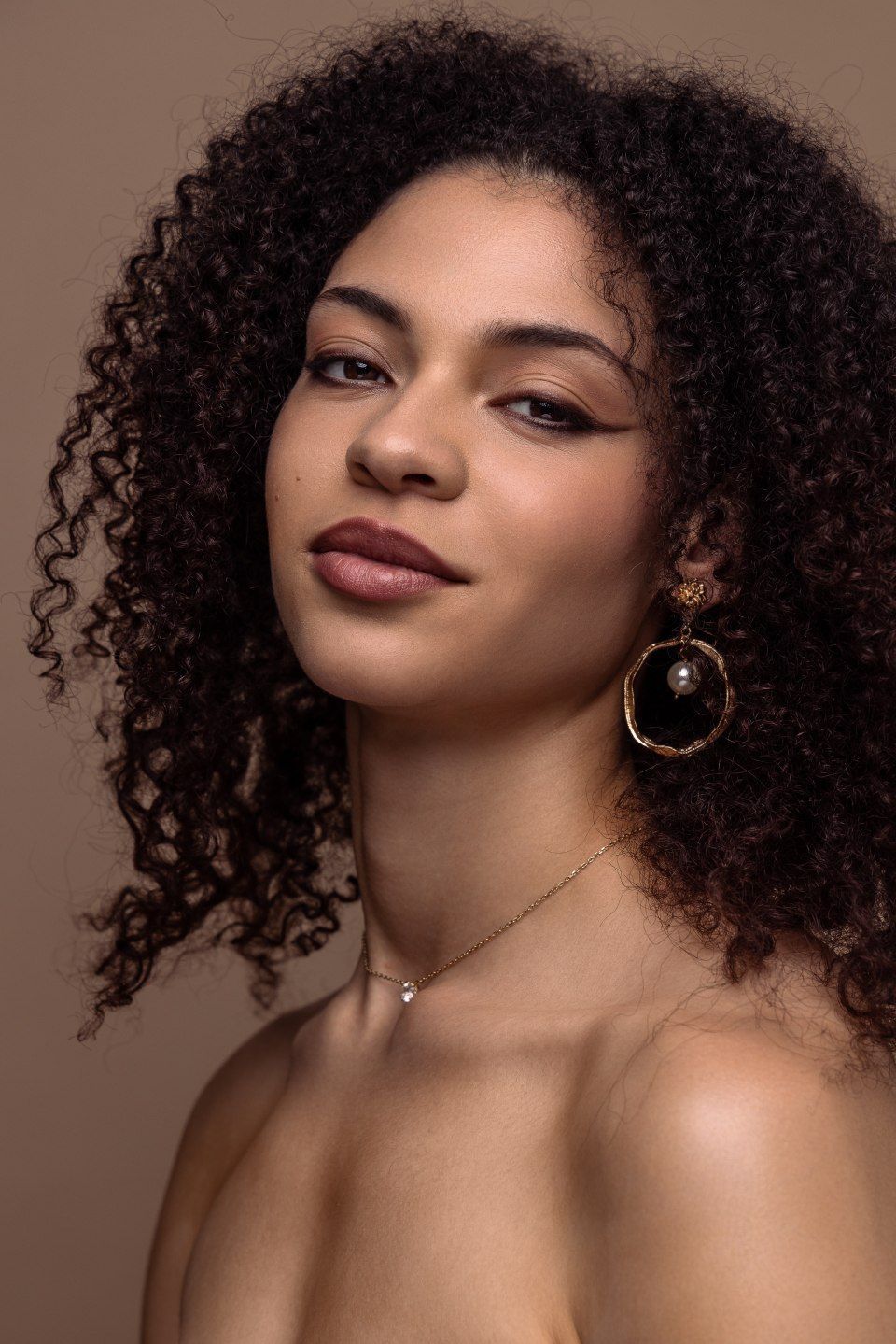 Eine Frau mit lockigem Haar trägt eine Halskette und Ohrringe.