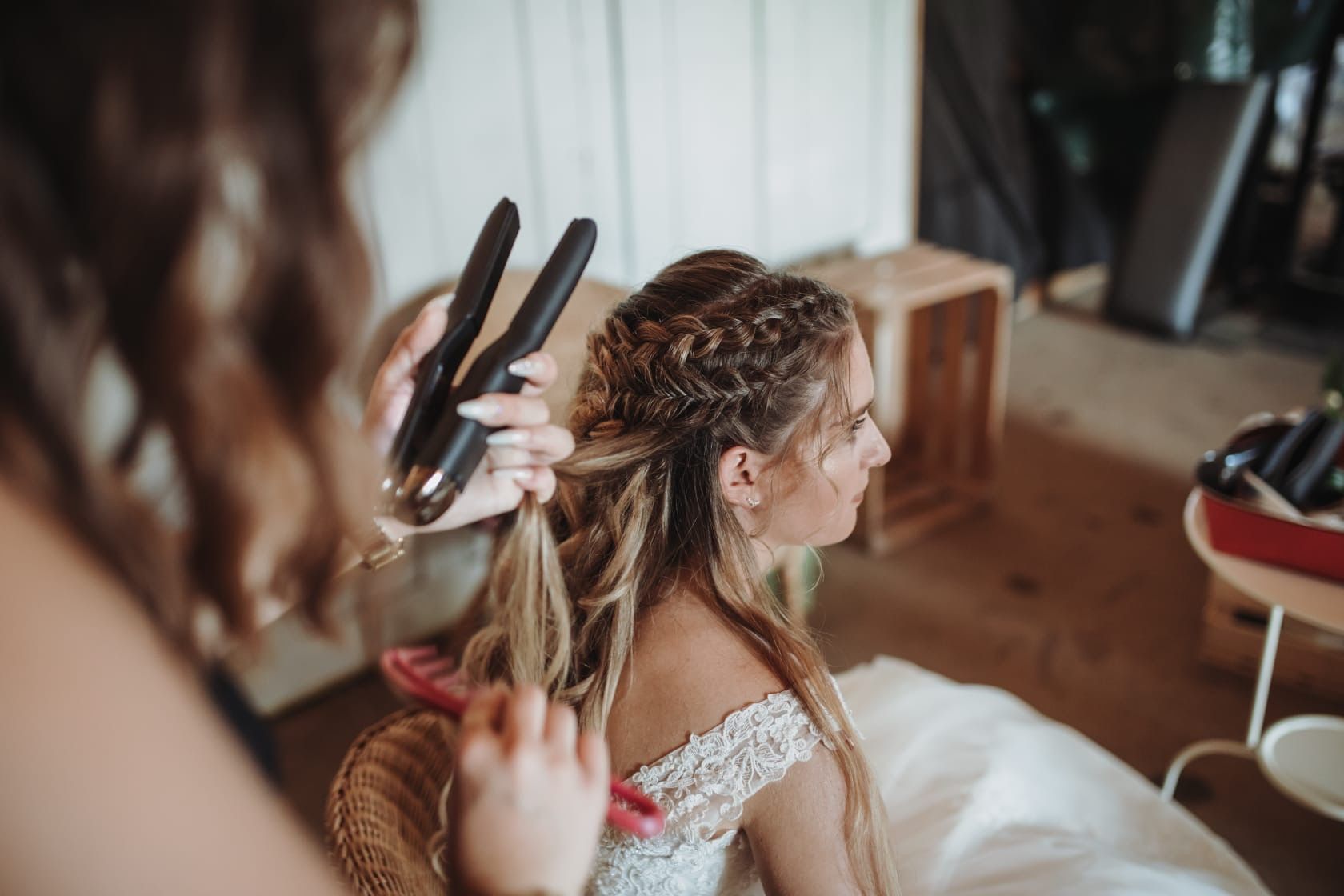 Eine Frau in einem Brautkleid lässt sich von einem Friseur die Haare glätten.