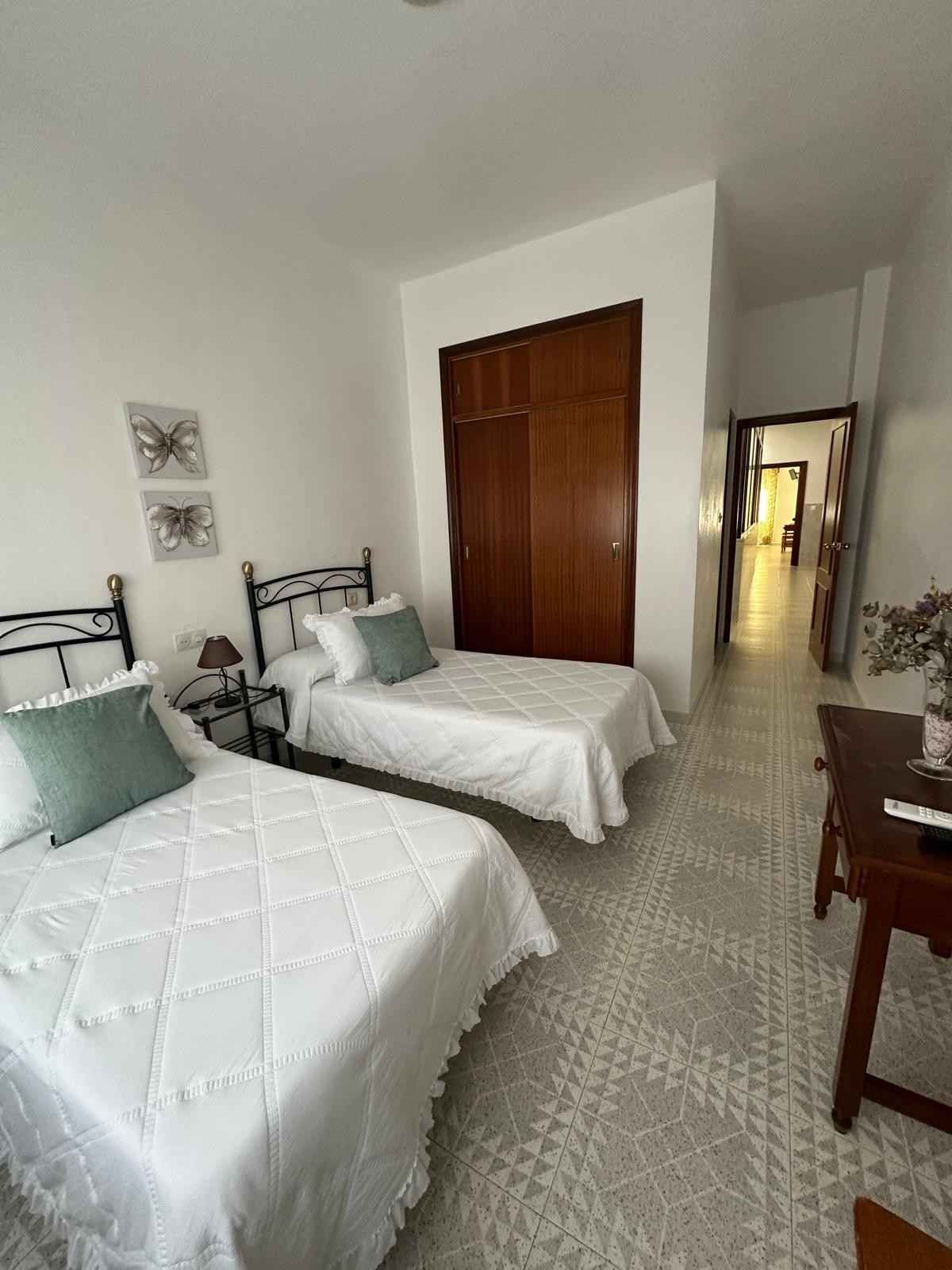 Habitación doble con ropa de cama blanca, armario de madera y escritorio junto a la pared.