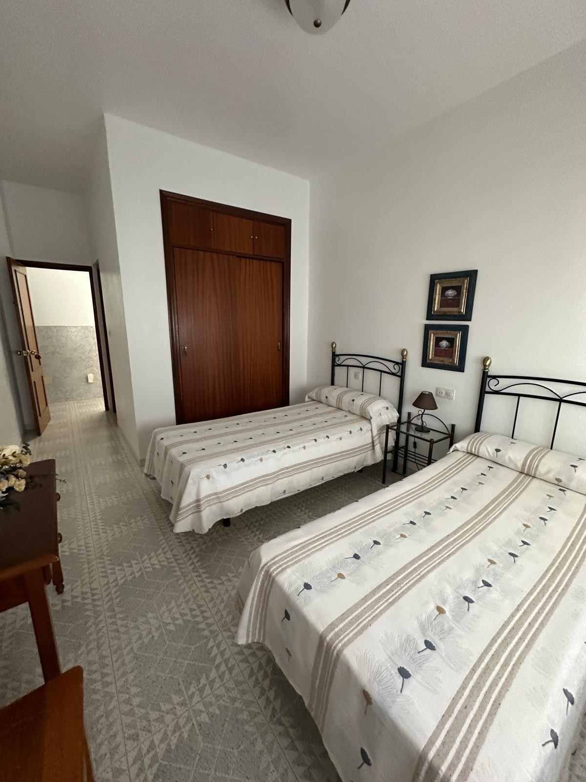 Habitación pequeña con dos camas individuales, paredes blancas, armario de madera y cuadros enmarcados.