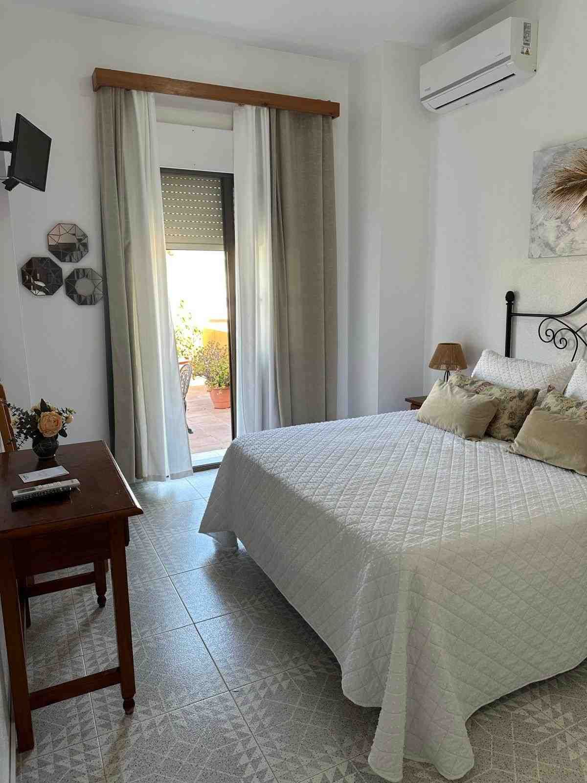 Habitación luminosa con cama, escritorio y puerta que da al balcón.
