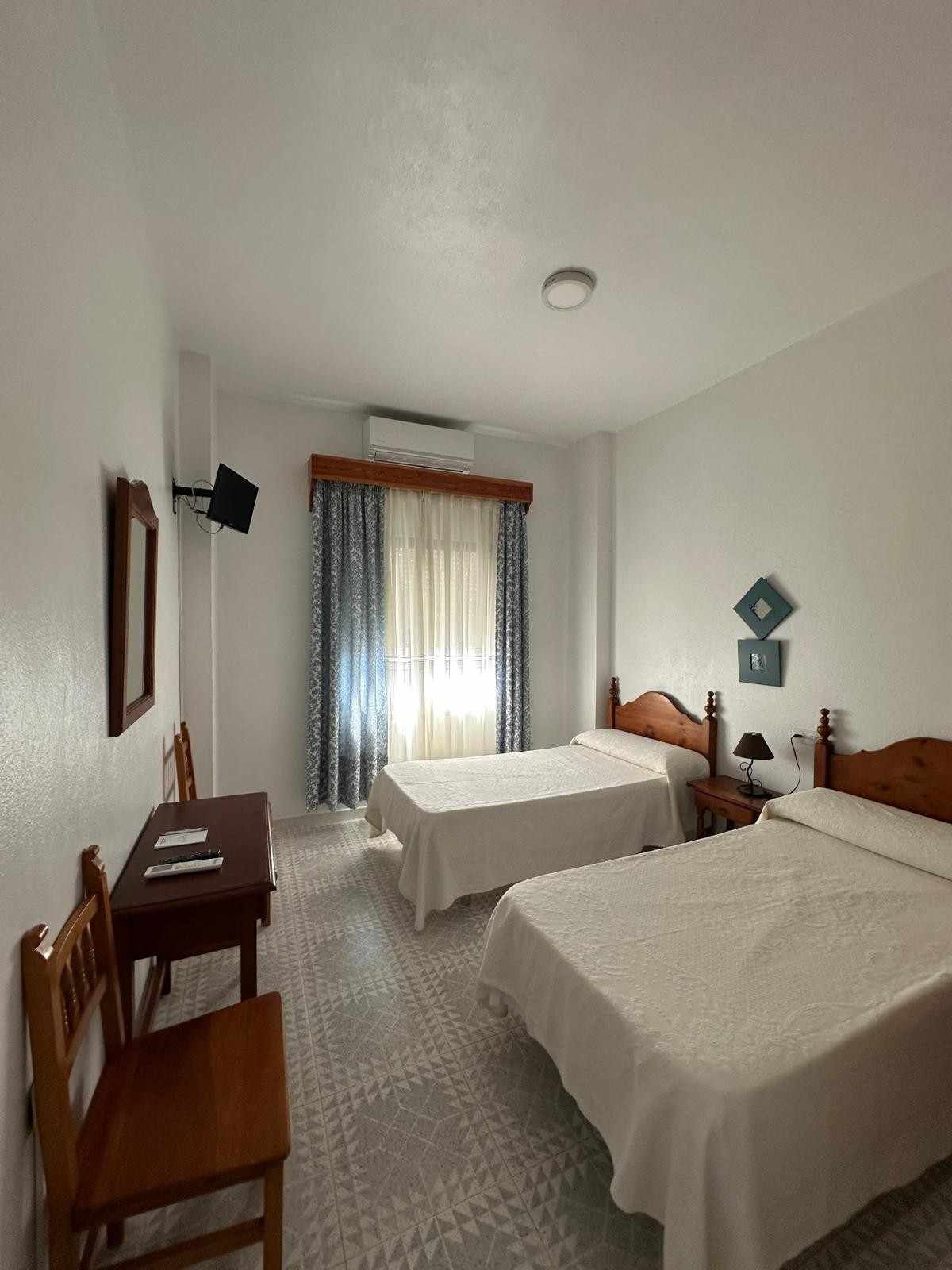 Habitación de hotel pequeña con dos camas individuales, escritorio, silla y ventana con cortinas.