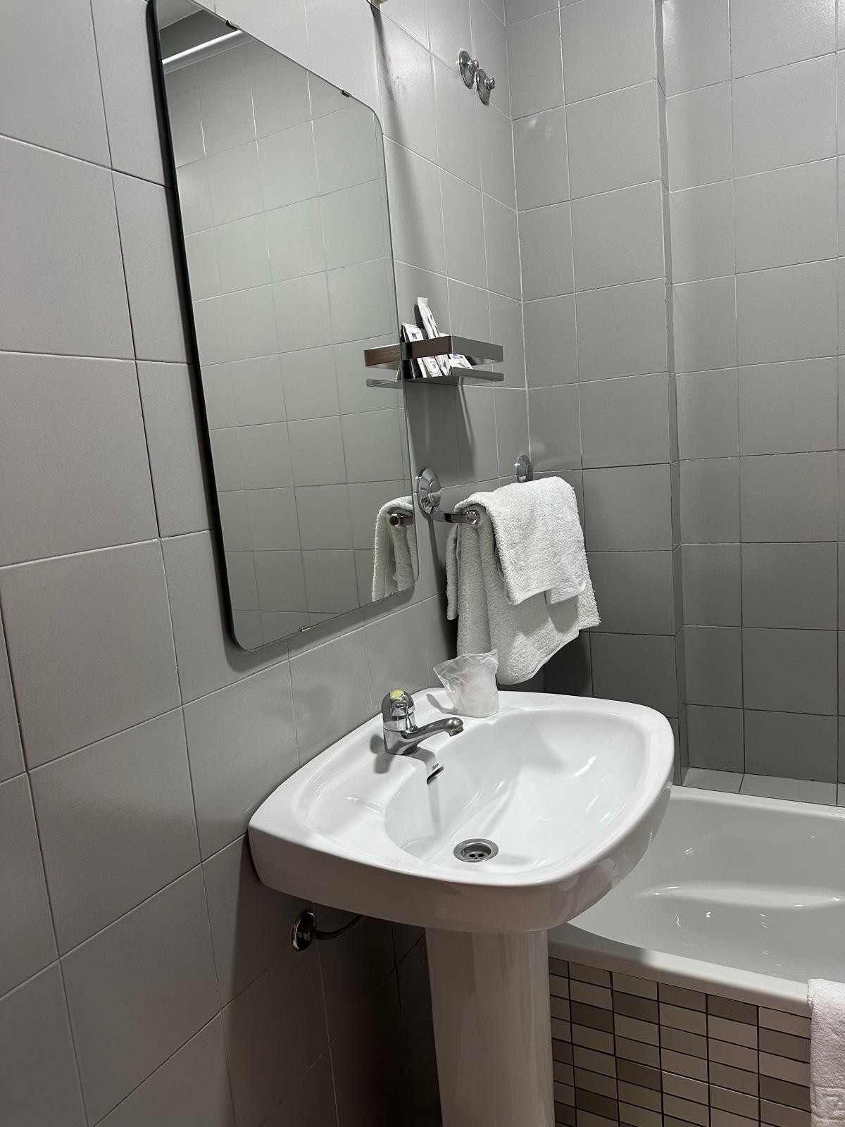Baño pequeño con azulejos, lavabo, espejo, grifo y una toalla colgada al lado.