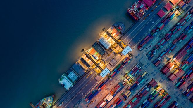 Ein Frachtschiff, ein Lastwagen und ein Flugzeug in einem Hafen bei Sonnenuntergang – Symbole für globalen Handel und Logistik.