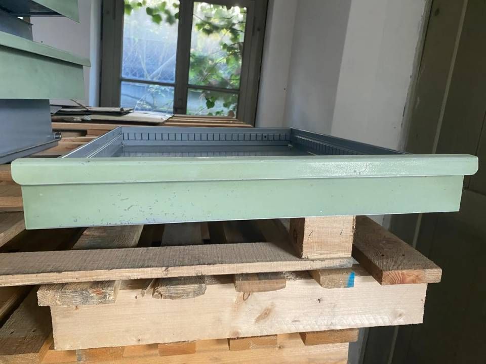 Ein hellgrüner Bienenstocksockel aus Holz mit Metalleinsatz, der auf gestapelten Holzpaletten steht.