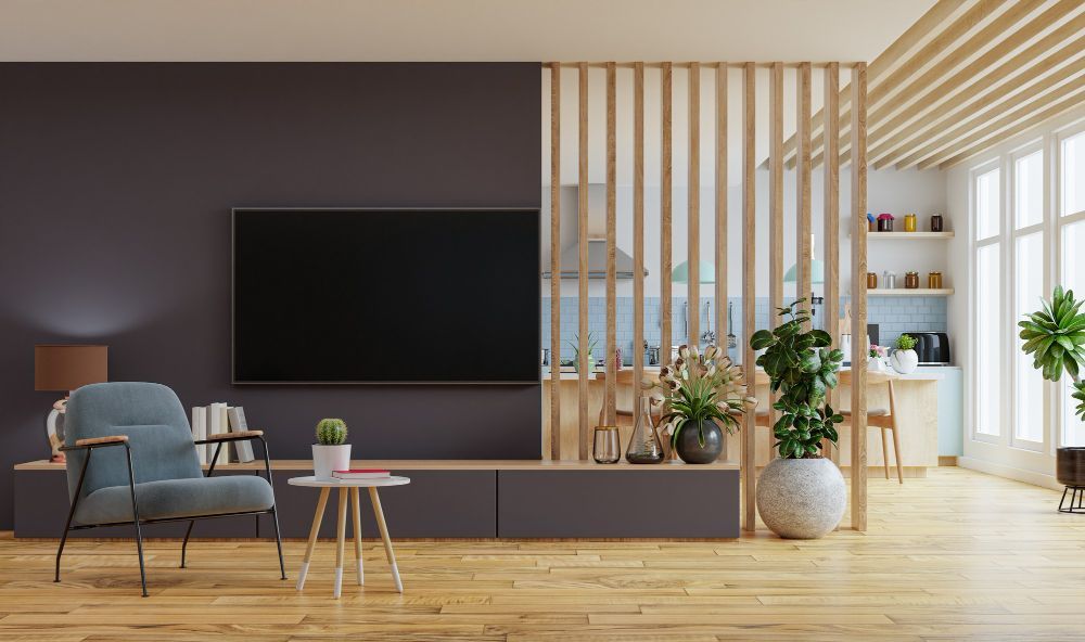 Sala de estar moderna con TV, sillón y biombo decorativo. Suelos de madera clara, pared oscura acentuada y plantas.