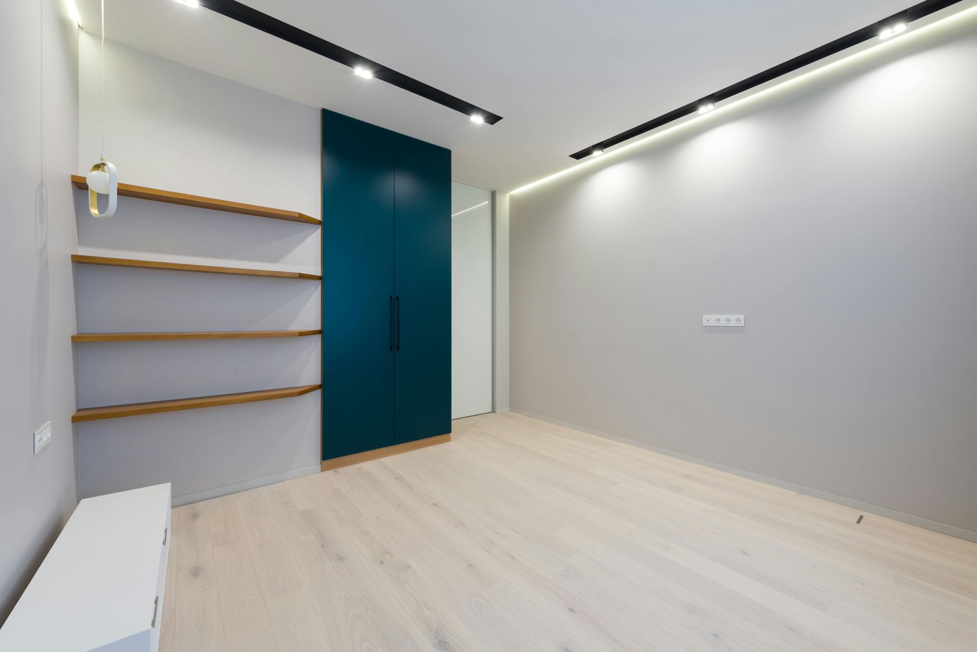 Una habitación vacía con suelos de madera, estantes y una puerta azul.