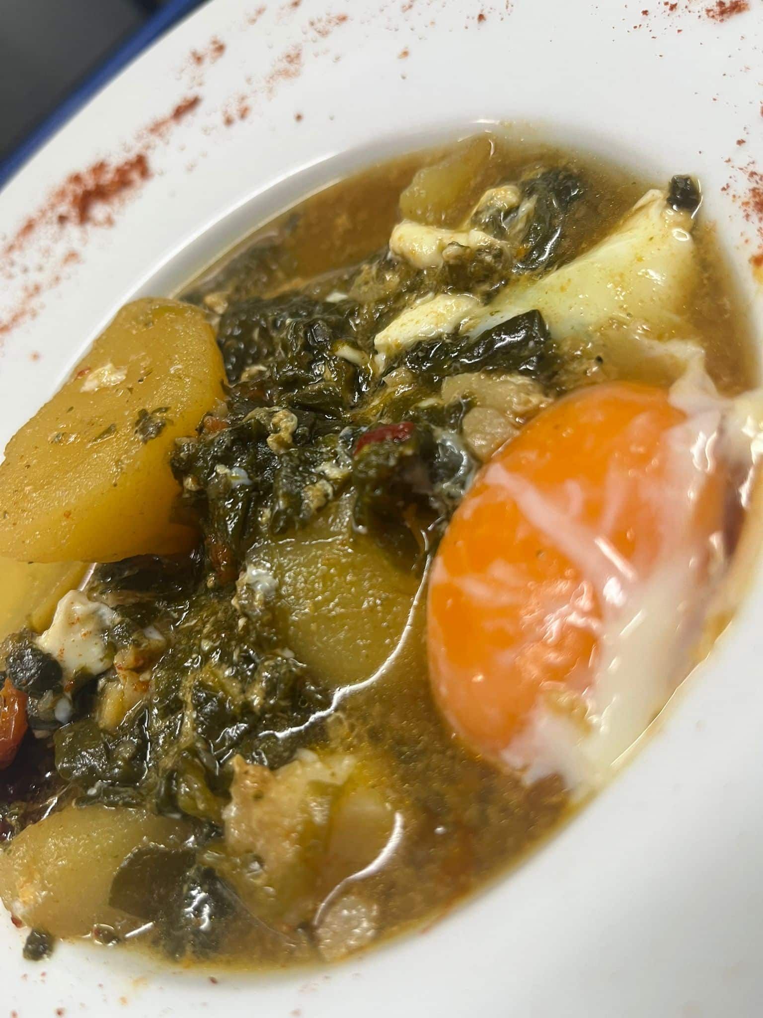 Sopa con patatas, verduras y un huevo escalfado con la yema líquida en un recipiente blanco.