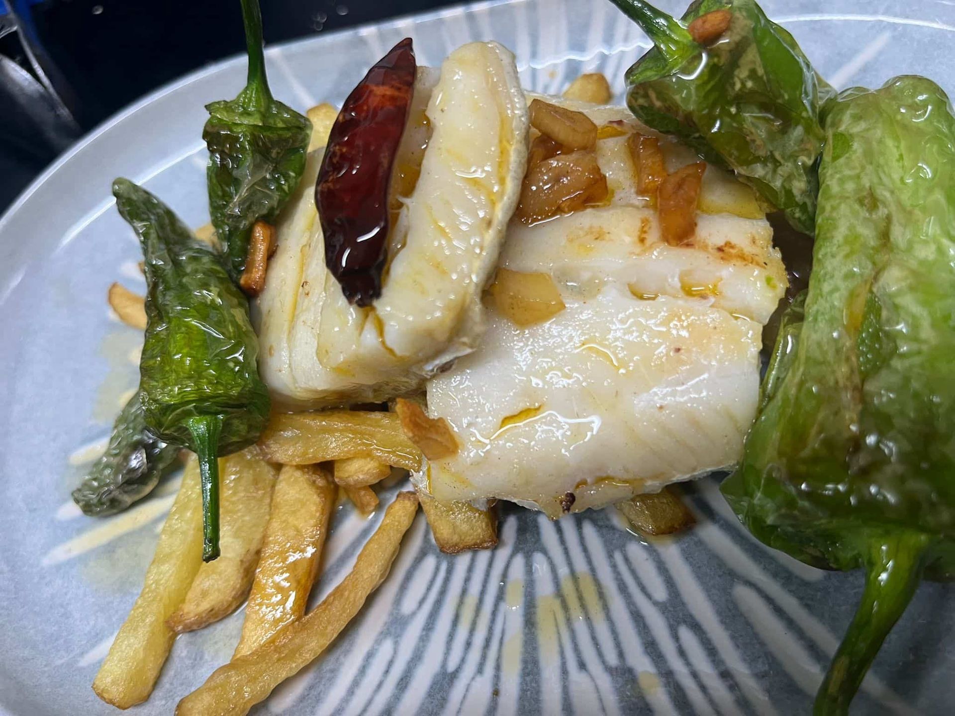 Filetes de bacalao con patatas fritas, pimientos fritos y ajo en un plato.