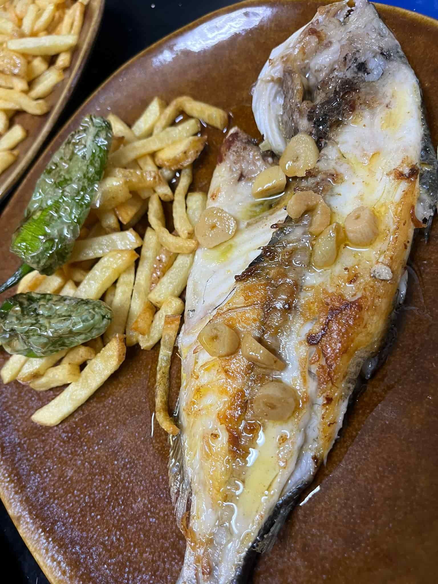 Pescado a la parrilla con ajo, patatas fritas y pimientos verdes en un plato marrón.