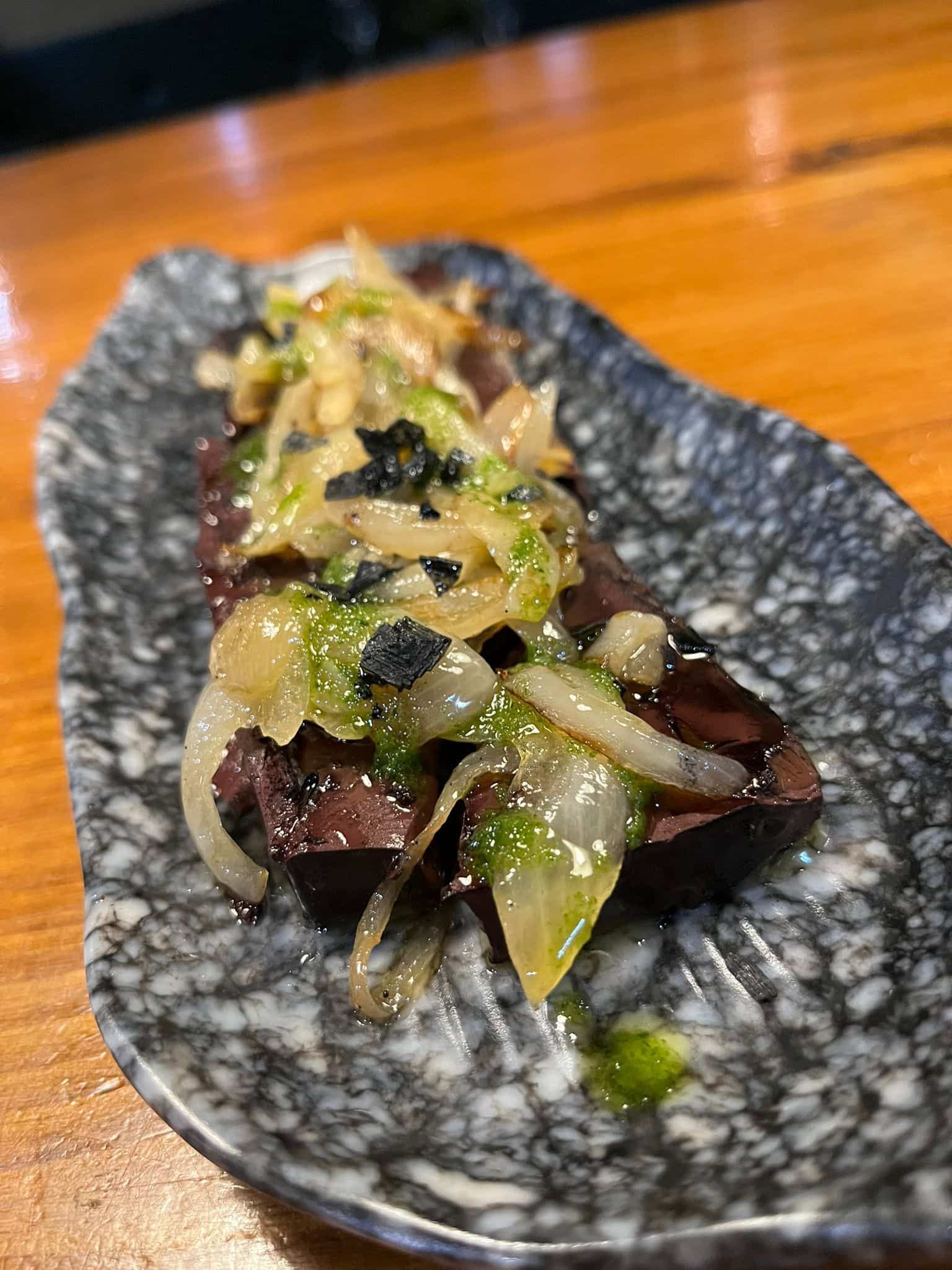 Carne a la parrilla cubierta con cebollas y verduras en un plato gris moteado.