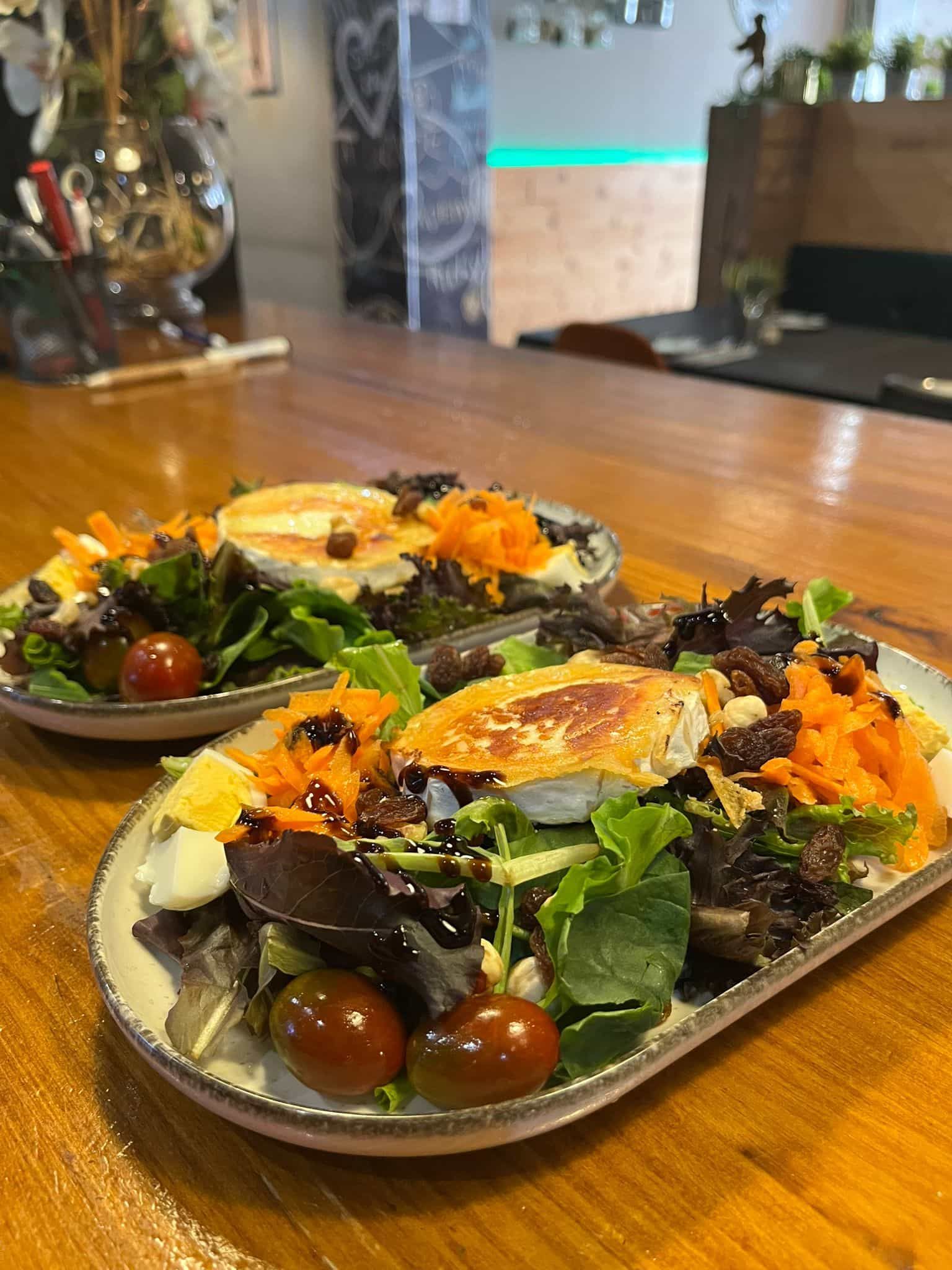 Dos ensaladas con queso frito, zanahorias y tomates en una mesa de madera.
