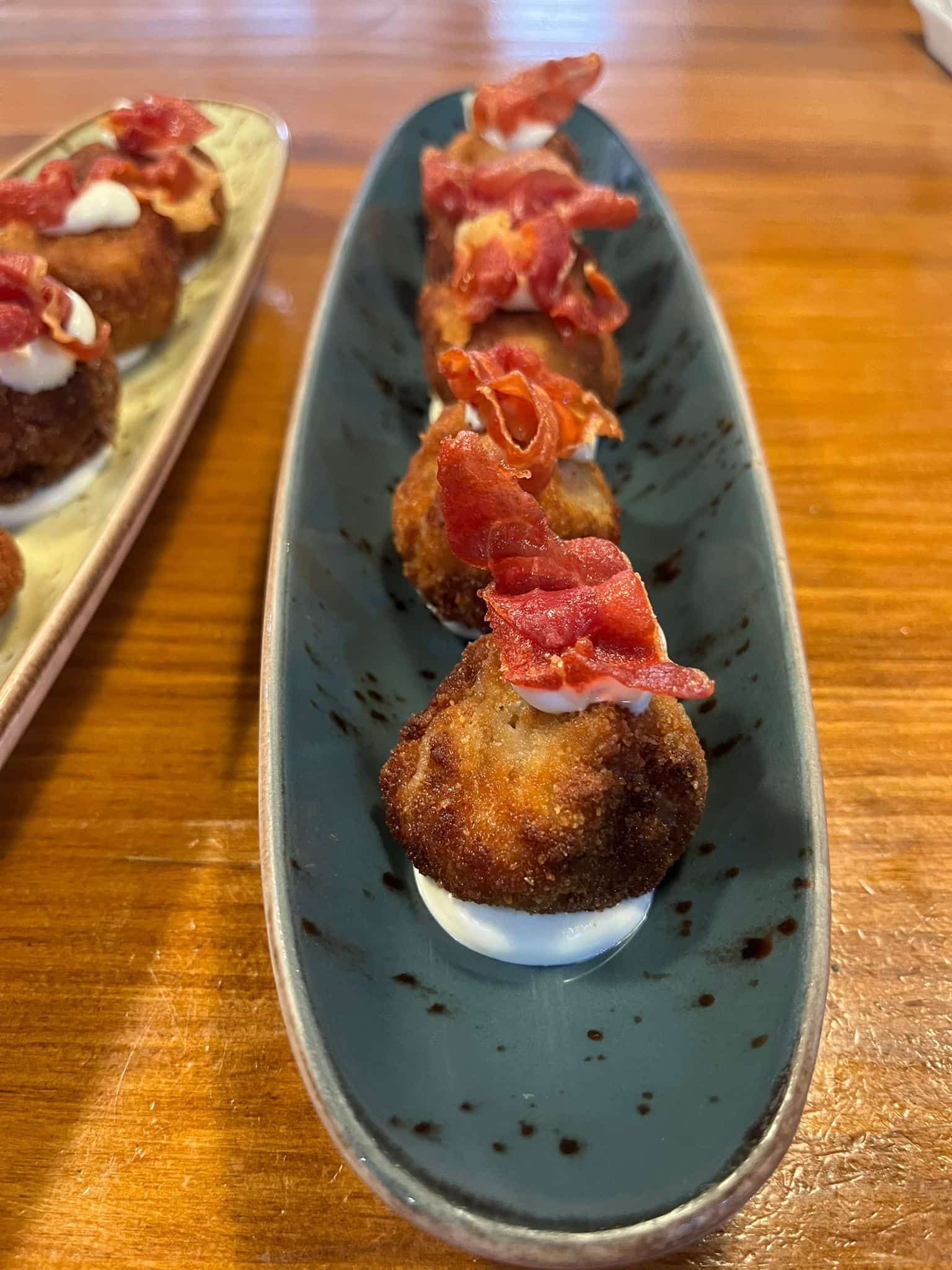 Bocados de comida frita cubiertos con carne y salsa, dispuestos en una bandeja azul.