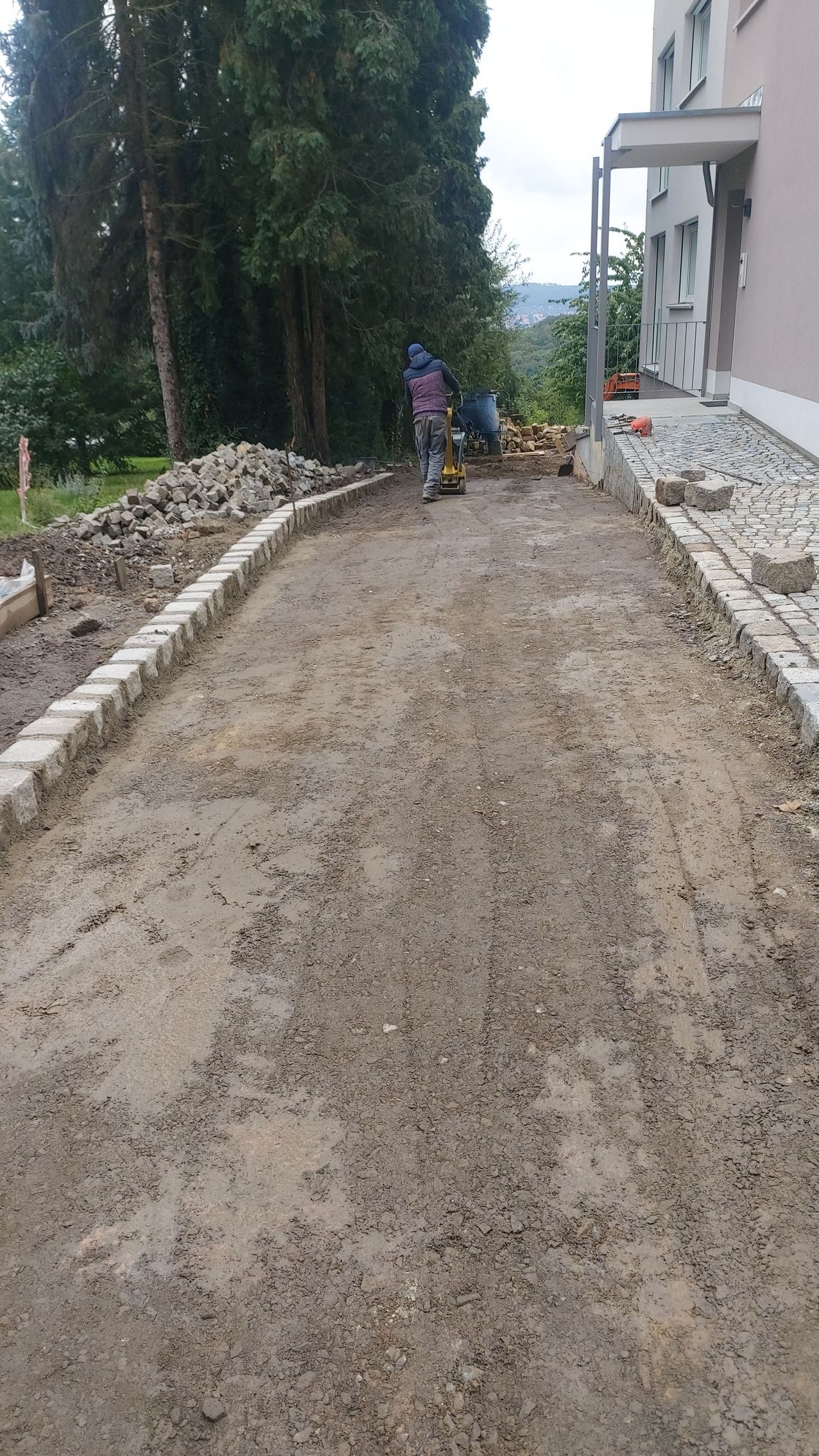 Baustelle: Weg mit Kies, gesäumt von Steinen. In der Ferne Arbeiter.