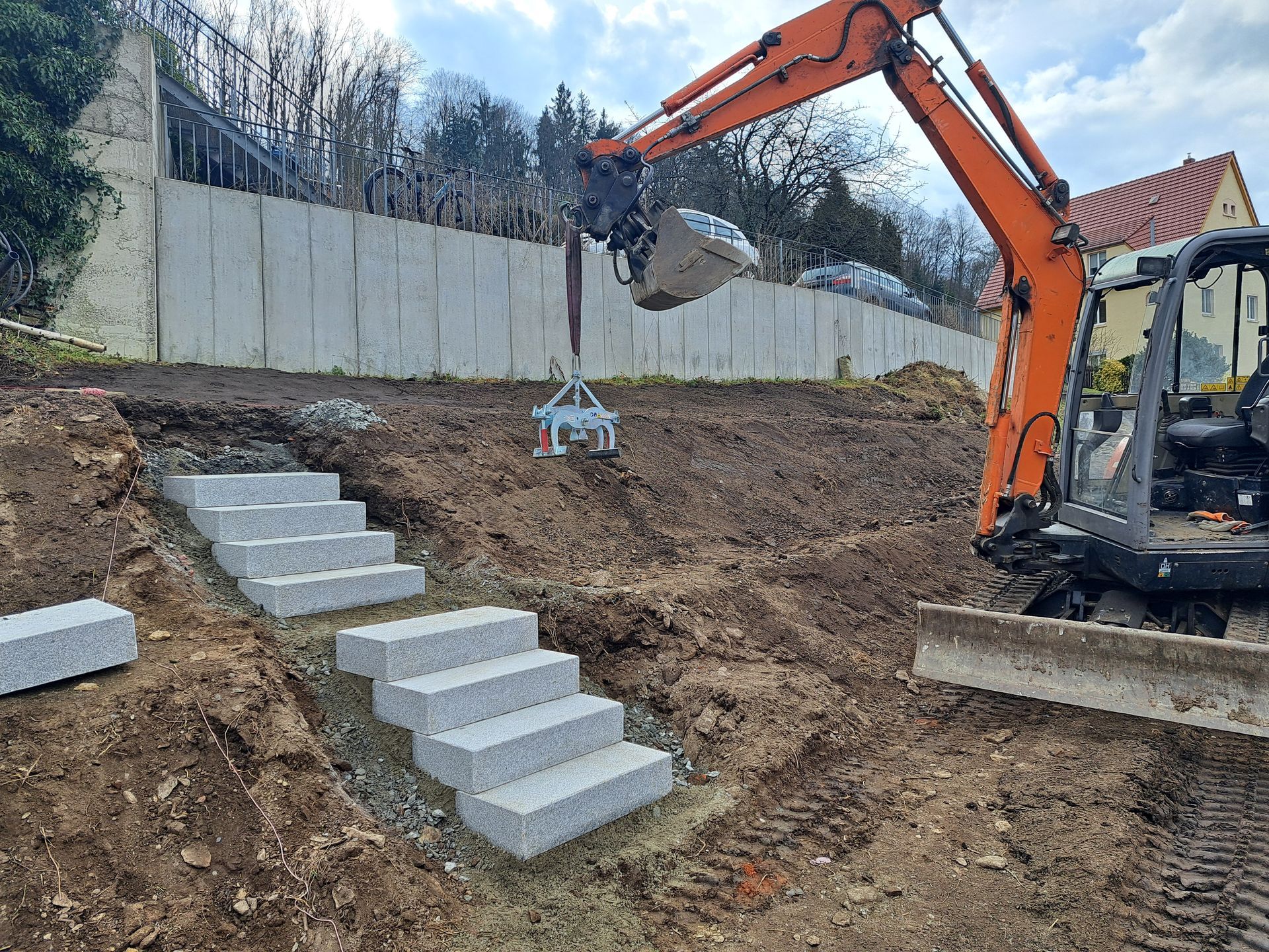 Ein Bagger platziert Steinstufen auf einer Baustelle am Hang.