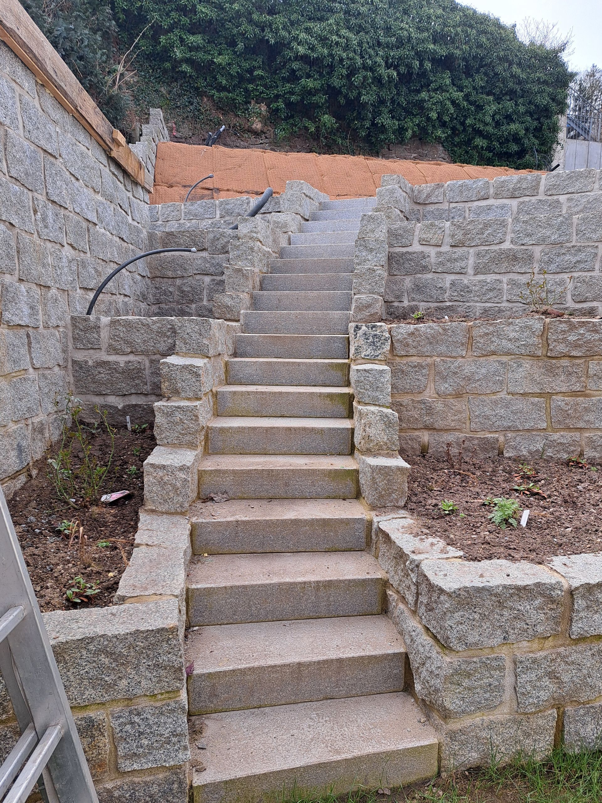 Steinstufen führen hinauf zu einem Terrassengarten mit Stützmauern und Grünanlagen.