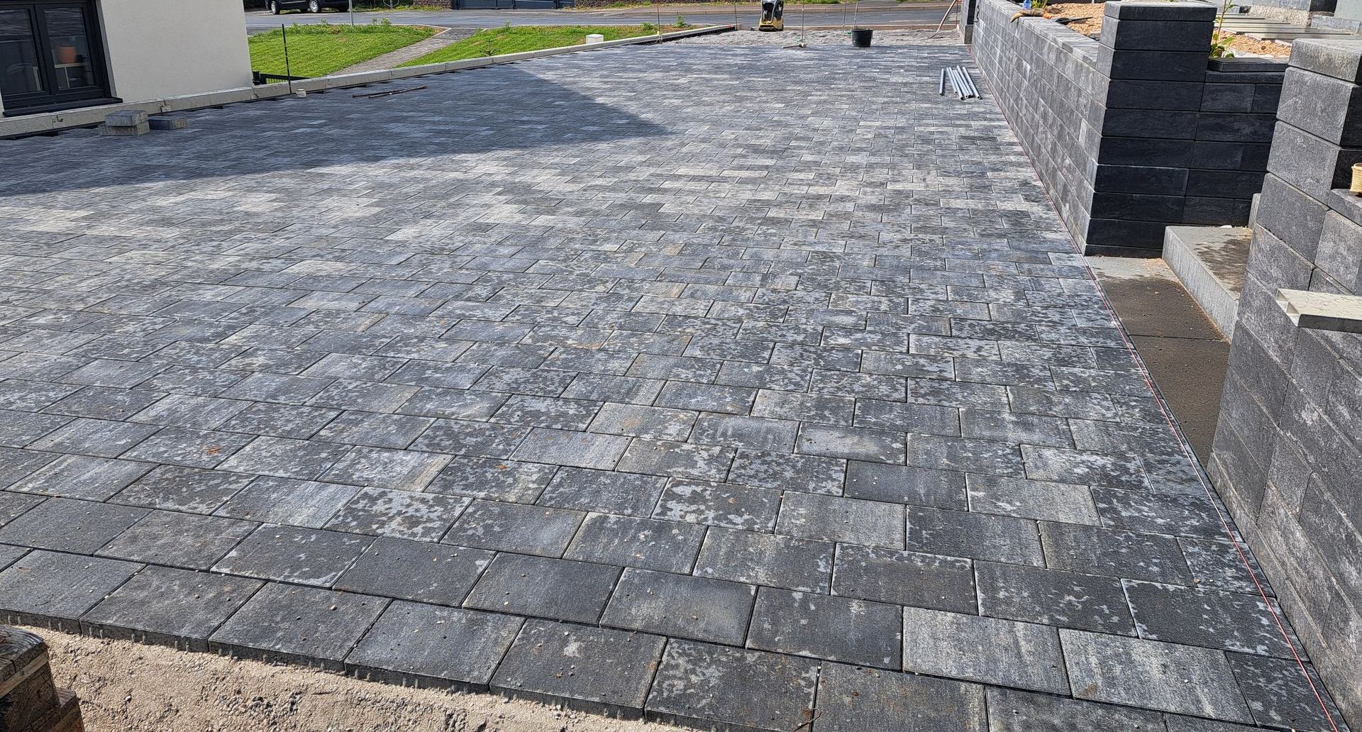 Graue Pflasterklinker in einer Einfahrt mit einer dazu passenden Steinmauer auf der rechten Seite.