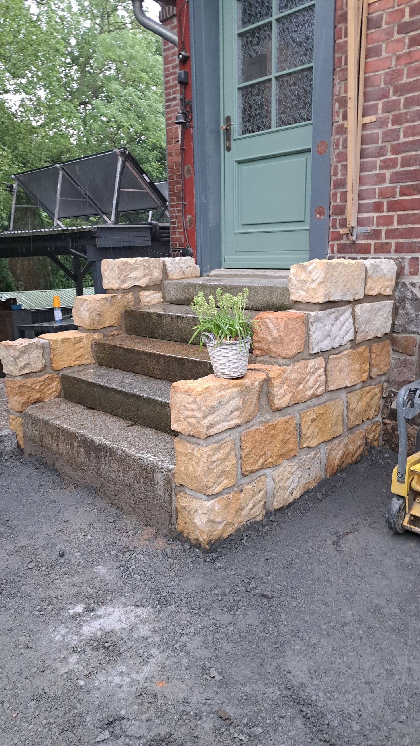 Steinstufen führen zu einer grünen Tür, die aus Blöcken gebaut ist. Auf der mittleren Stufe steht eine Topfpflanze.