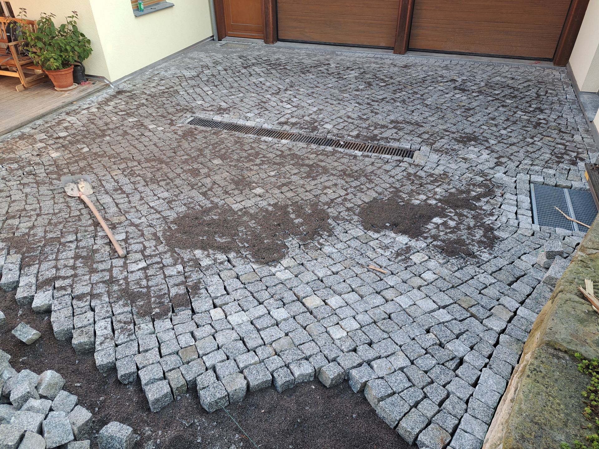 Kopfsteinpflasterauffahrt im Bau, mit Entwässerungssystem. Eine Schaufel liegt auf dem Boden.