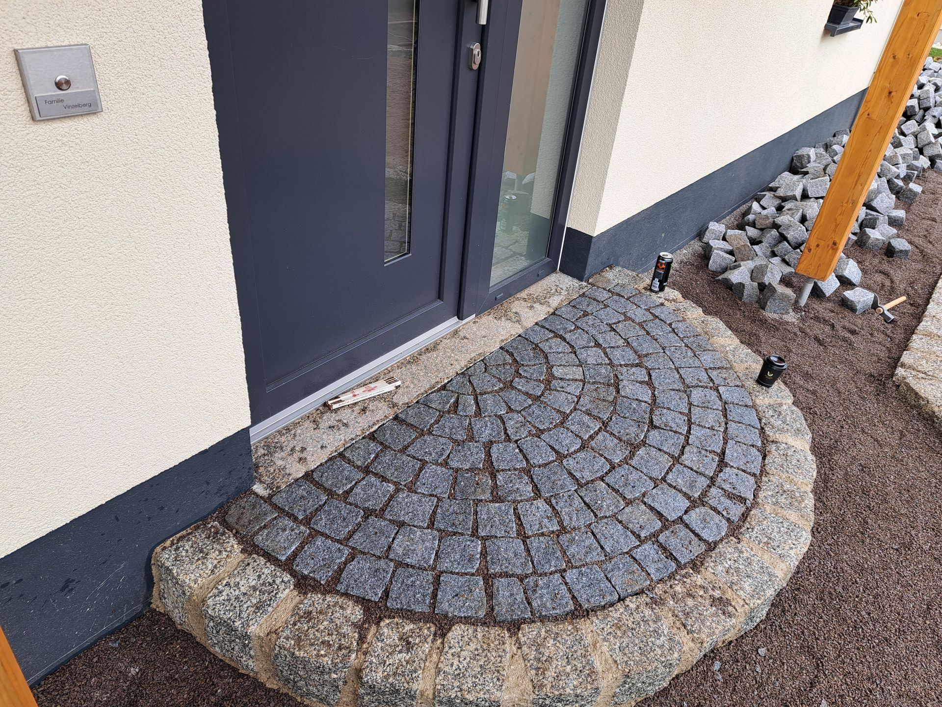 Halbrunder Steineingang mit grauem Kopfsteinpflaster, der zu einer dunkelgrauen Tür führt.