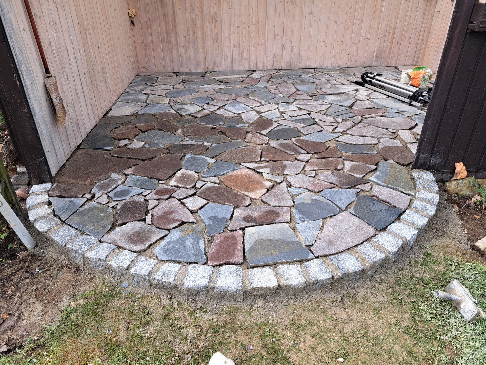 Steinterrasse mit geschwungenem Rand, aus flachen Steinen in verschiedenen Farben.