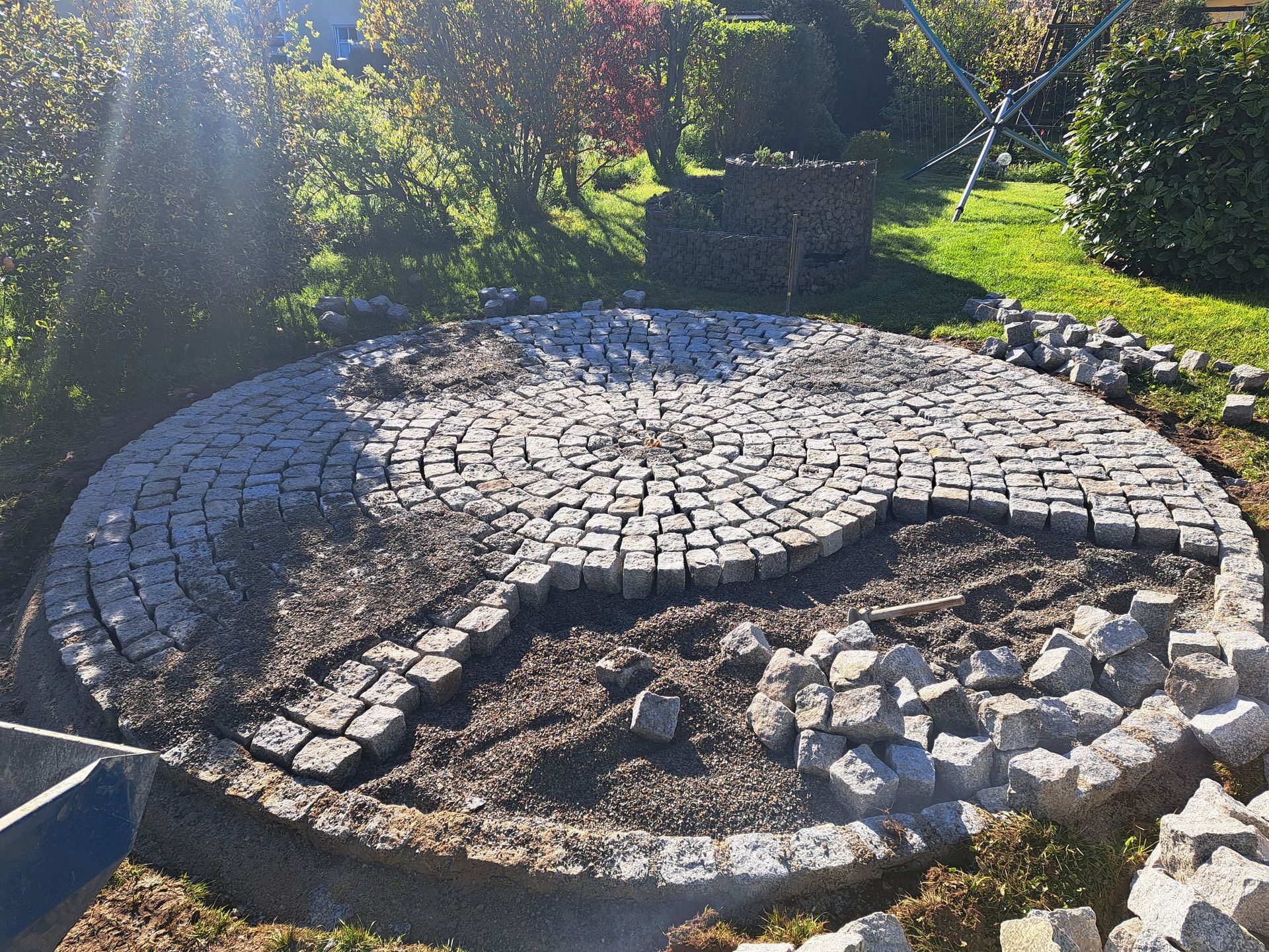 Im Bau befindliche runde Terrasse mit Kopfsteinpflaster, Erde und umgebender Landschaftsgestaltung.