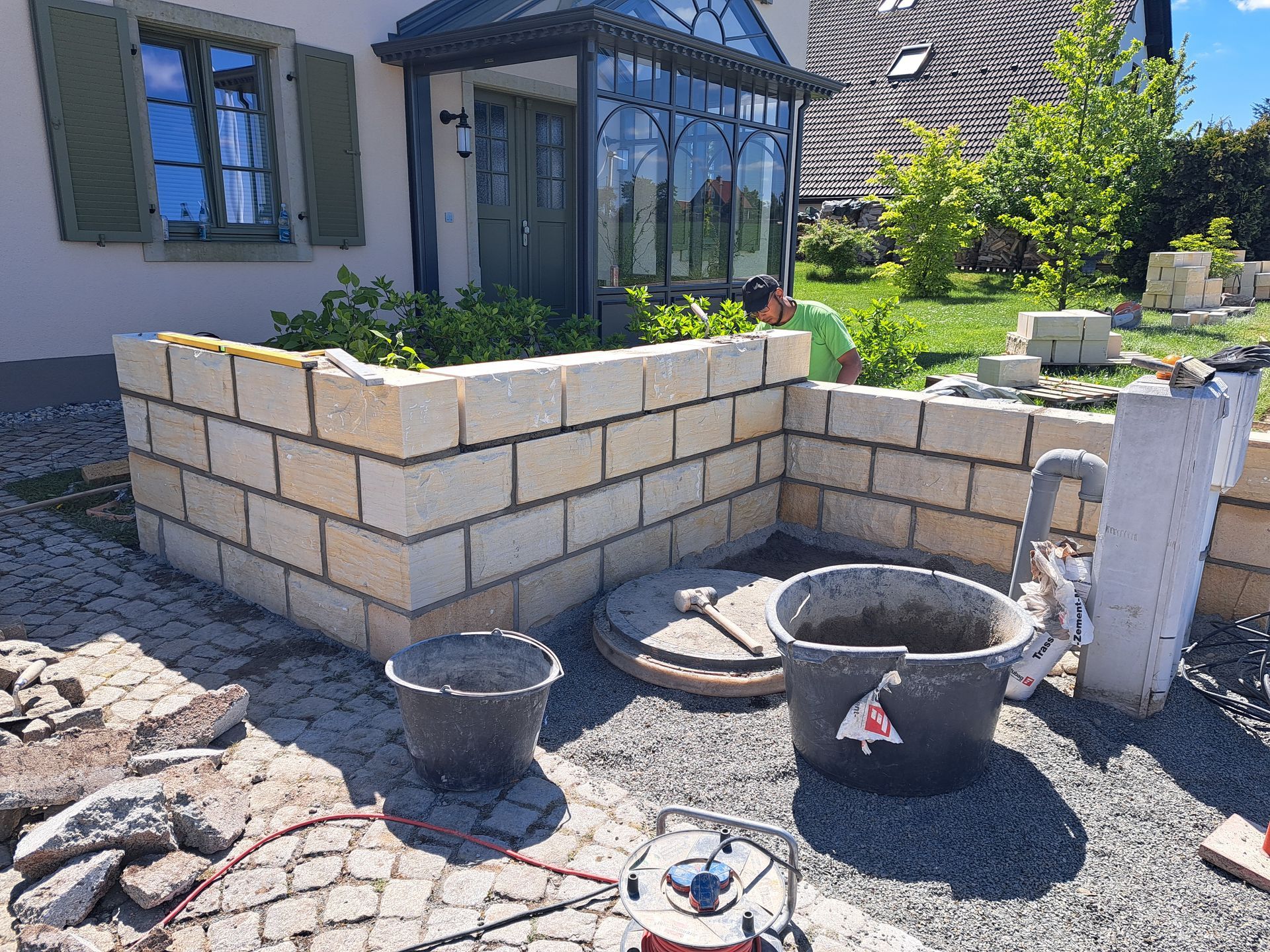 Eine im Bau befindliche Ziegelmauer in einem Garten, mit einem Arbeiter.