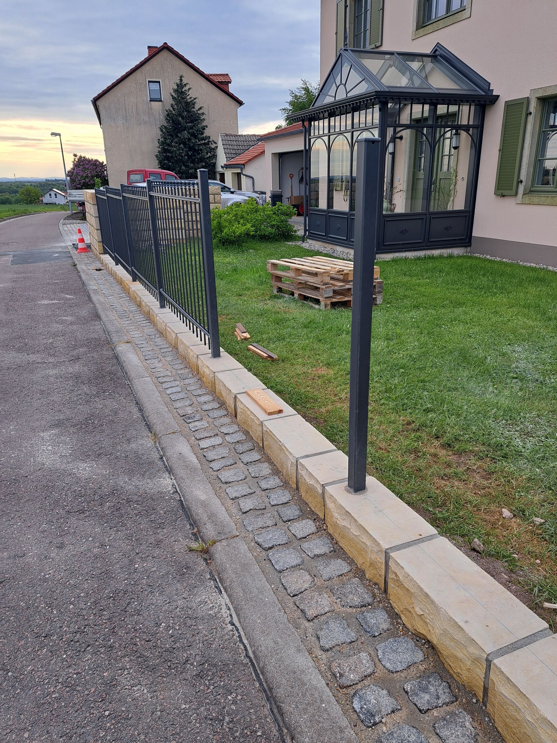 Schwarzer schmiedeeiserner Zaun entlang eines Gehwegs neben einem grasbewachsenen Hof. 