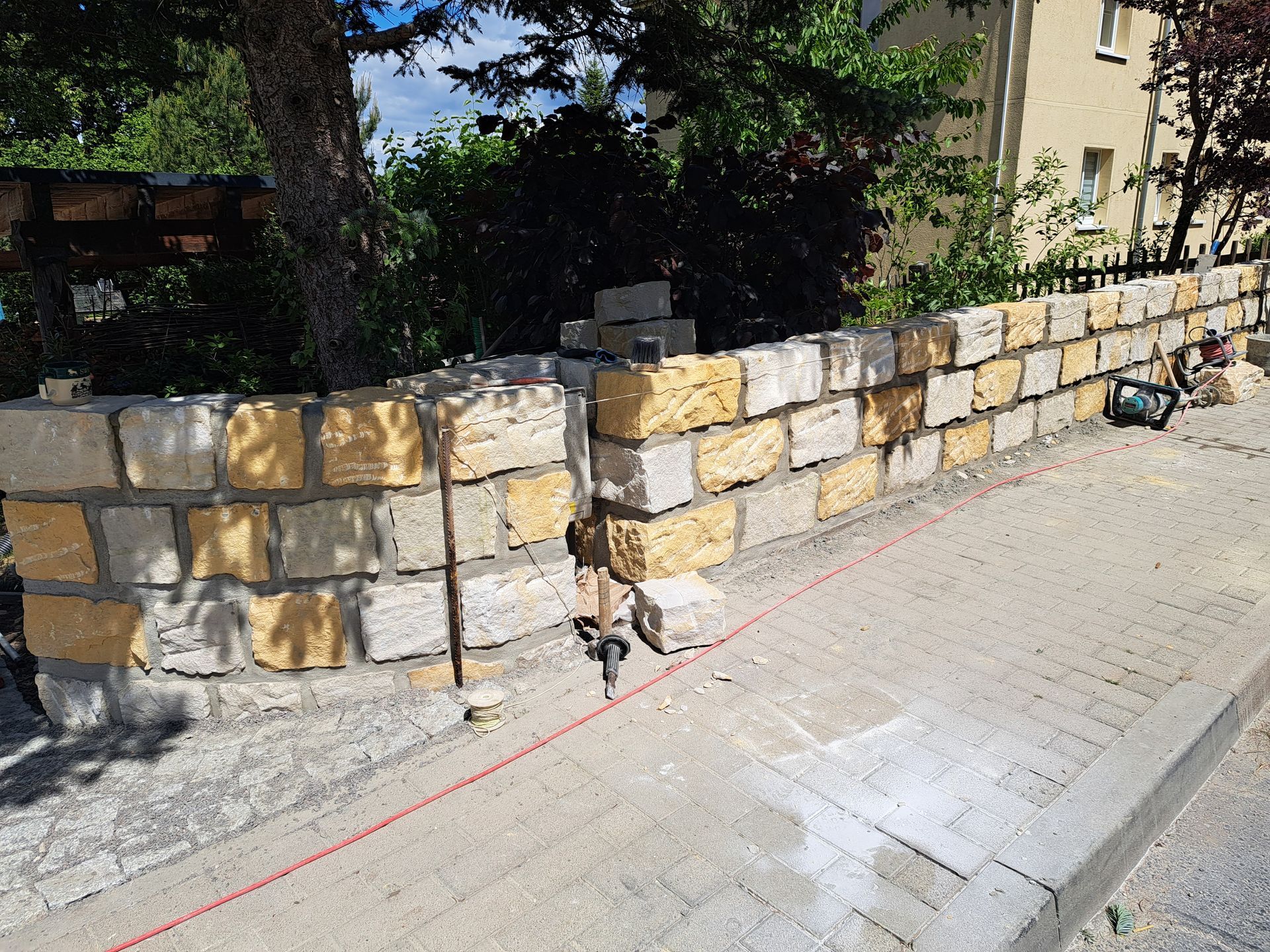 Bau einer Steinmauer im Freien, mit gelben und grauen Blöcken, unter einem Baum.
