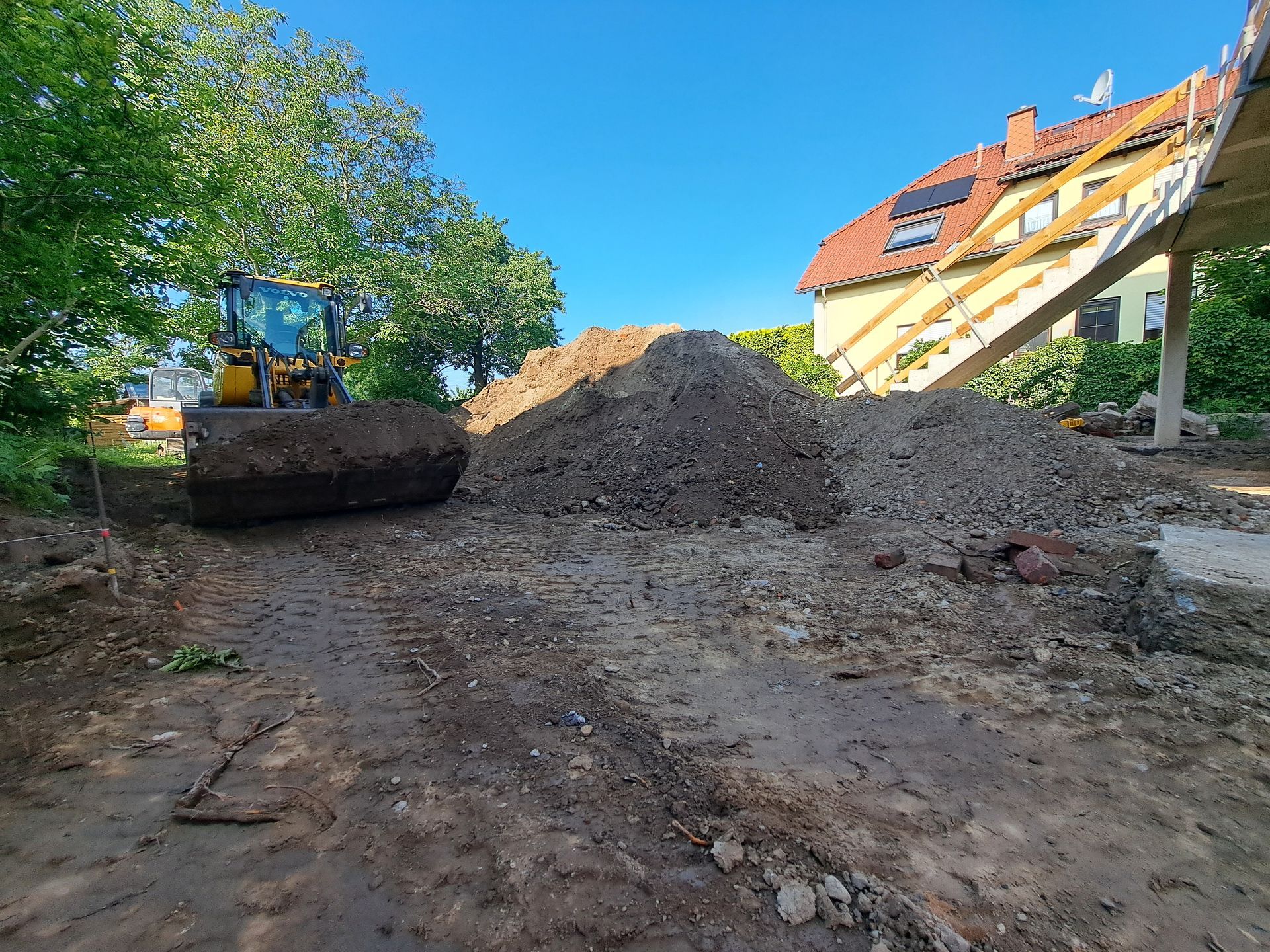 An einem sonnigen Tag lädt ein Bagger Erde neben einem im Bau befindlichen Haus.