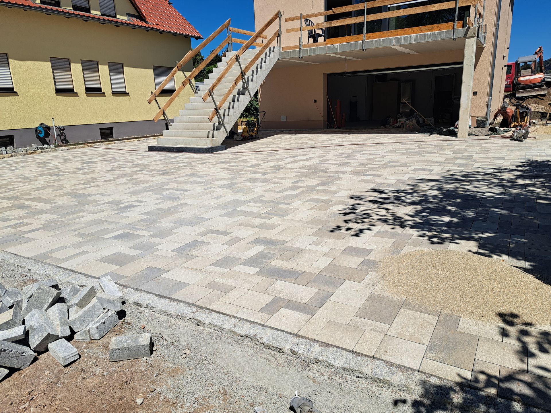 In einer Einfahrt werden Pflastersteine ​​verlegt, eine Treppe führt zu einem Gebäude und ein Stapel Betonblöcke.